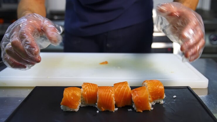 Chef in restaurant prepares sushi rolls with salmon, rice and and avocado. Cook`s hands putting sushi rolls on the mat. Delicious asian food.