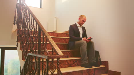 businessman typing on smartphone sitting on stairs