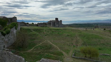 ancient ruins in scodra with open green fields and distant mountains under cloudy skies