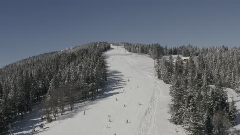 kope ski resort slovenia with skiers going downhill at ribnica one track, aerial approach shot