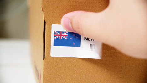 Hands-applying-MADE-IN-NEW-ZEALAND-flag-label-on-a-shipping-cardboard-box-with-products