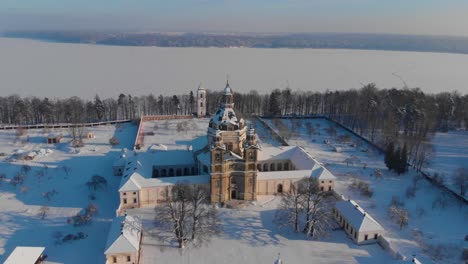 Aerial-view-of-the-Pazaislis-monastery-and-the-Church-of-the-Visitation-in-Kaunas,-Lithuania-in-winter,-snowy-landscape,-Italian-Baroque-architecture,-flying-around-the-tower,-lake-in-the-background