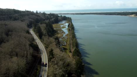 us, oregon, garabaldi, nehalem bay, 2025-03-18 - drone view over the railroad along nehalem bay with the pacific ocean in the distance. the railroad is on a berm.