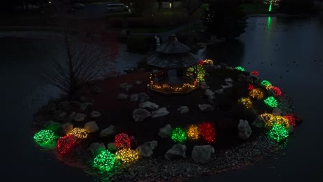 green, red, yellow christmas lights in garden with pond during december night in usa