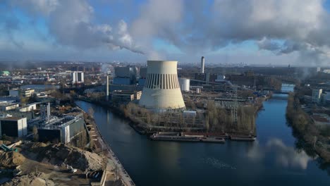 power plant emitting steam from its cooling tower, situated by a river and overlooking the cityscape. magic aerial view flight panorama orbit drone