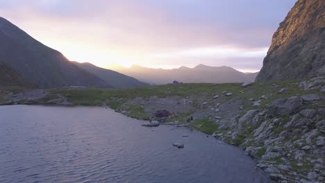 Aerial-view-of-peaceful-mountain-lake-at-sunset-with-dramatic-purple-and-red-sky-over-distant-peaks