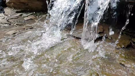 flowing-waterfall-from-a-mountain-spring-stream-running-down-huge-sandstone-slabs-of-rock-with-green-moss,-crystal-clear-drinking-water,-meditate-tranquil-and-peaceful-calm-slow-motion