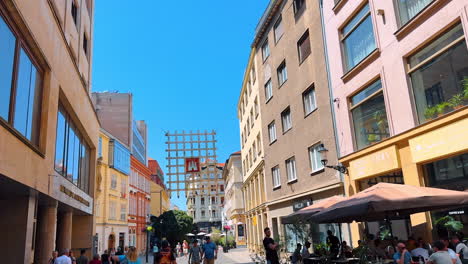bratislava, slovakia - june 5, 2025: sunny city strolls happening!. people stroll through a vibrant urban street lined with shops and cafes under a clear blue sky