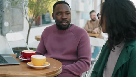 hombre afroamericano hablando con una colega en una pausa para el café en una cafetería al aire libre