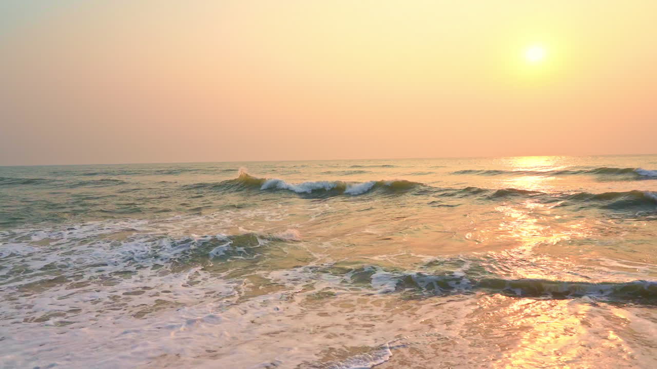 Static slow-motion shot of the sea waves hitting the sandy tropical beach during sunset