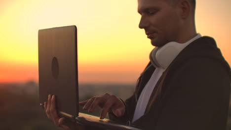 estar de pie al atardecer en el techo con una computadora portátil y cerveza en auriculares trabajar remotamente y contemplar la belleza. estar en armonía trabajar de forma remota con su computadora portable.
