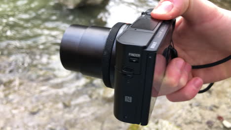 a compact camera unfolds its lens, seen from above on the edge of a swiss river, technology