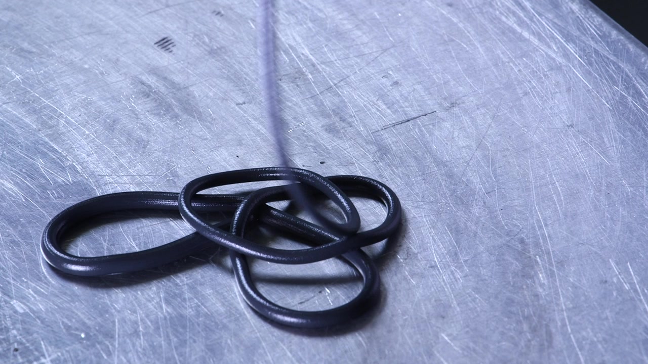 Close-up van een polymeerfilament dat uit industriële apparatuur komt tijdens een extrusieproces. Ideaal voor productie, kunststoftechniek en industriële productieconcepten