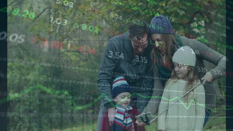 animation of graphs and trading board over caucasian woman taking selfie with family using cellphone