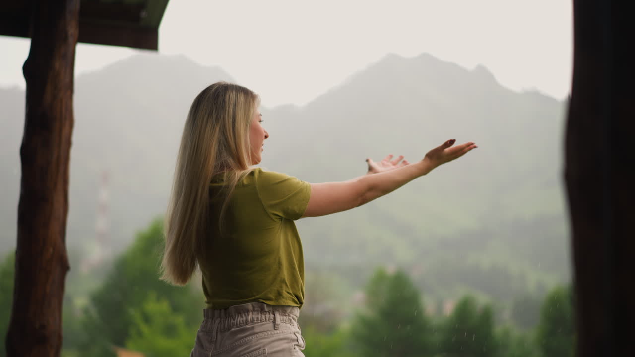 즐거운 여자가 여름 비방울 아래 열려있는 손바닥을 들고 있습니다.