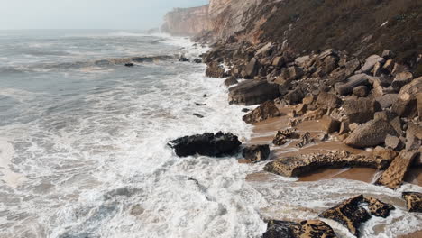 aerial footage capturing the unyielding force of sea waves crashing against the rugged coastal expanse of nazare, portugal