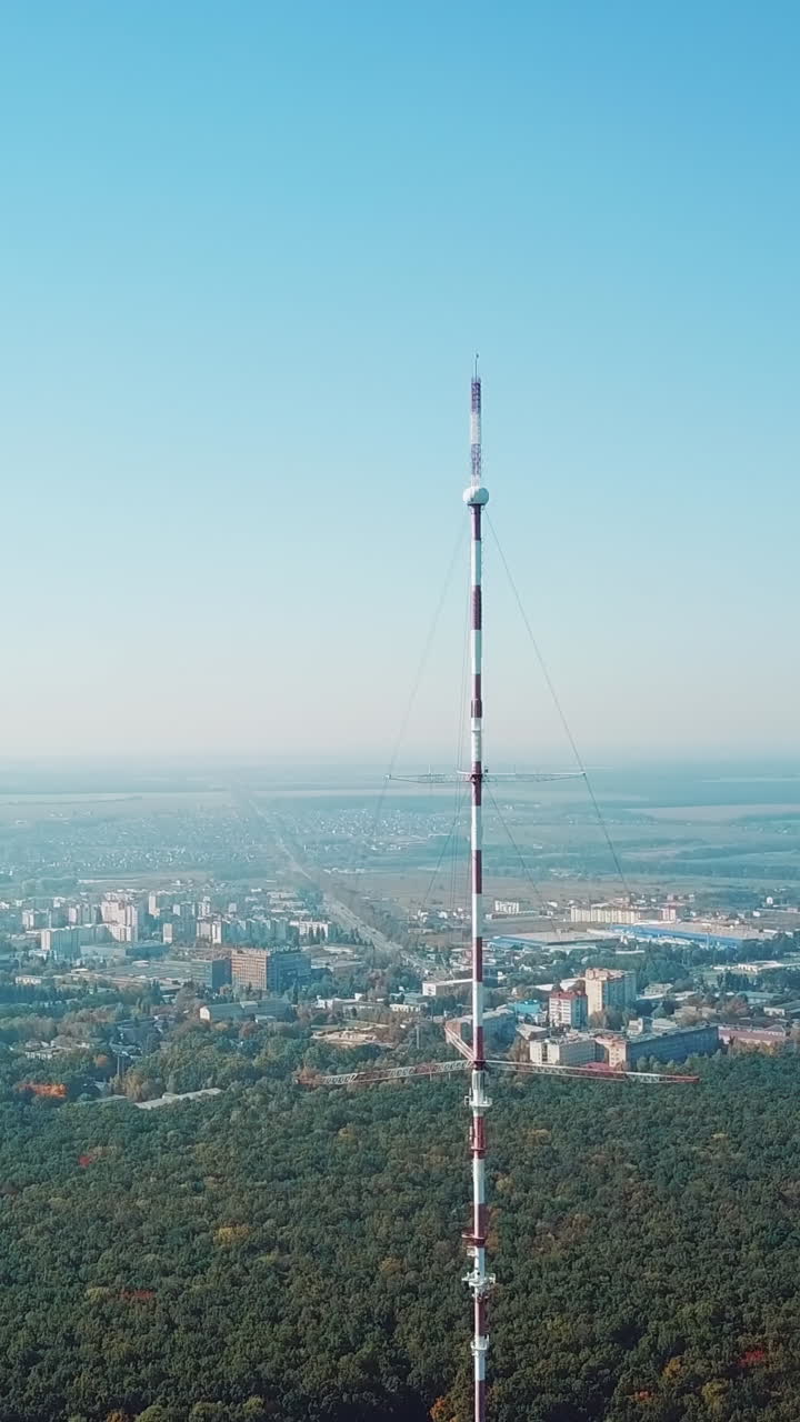 top of the telecommunication tower in red and white colours on the background of the cityscape and blue sky. Camera motion up Vertical video