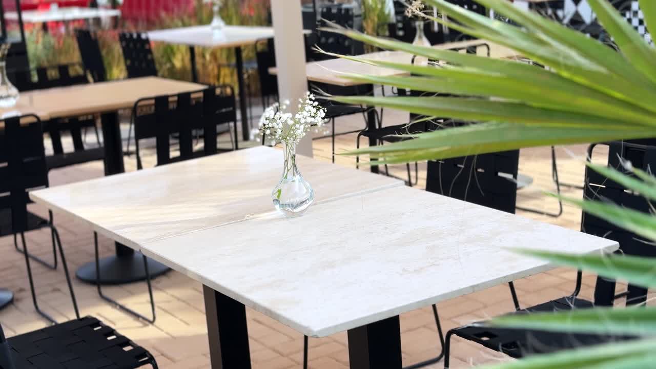 upscale outdoor restaurant or cafe patio featuring light marble tables and black metal seating under bright daylight.A small flower vase adds a minimalist touch.Ideal for showcasing commercial spaces,