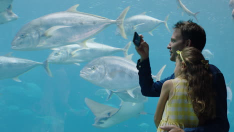 padre con su hija en el acuario tomando fotos de peces usando un teléfono inteligente disfrutando de la vida marina nadando en el tanque divirtiéndose en el oceanario compartiendo en las redes sociales