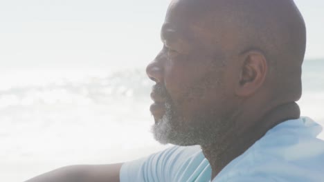 Senior-african-american-man-wearing-white-tshirt-sitting-on-sunny-beach