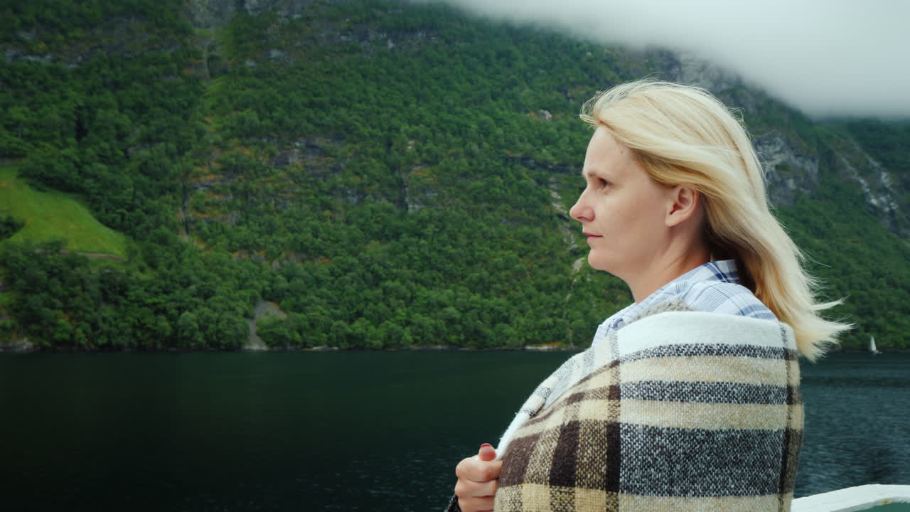 una mujer con una taza de té en las manos a bordo de un crucero mira las hermosas montañas de la