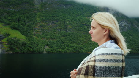 a woman with a cup of tea in her hands aboard a cruise ship looks at the beautiful mountains of the