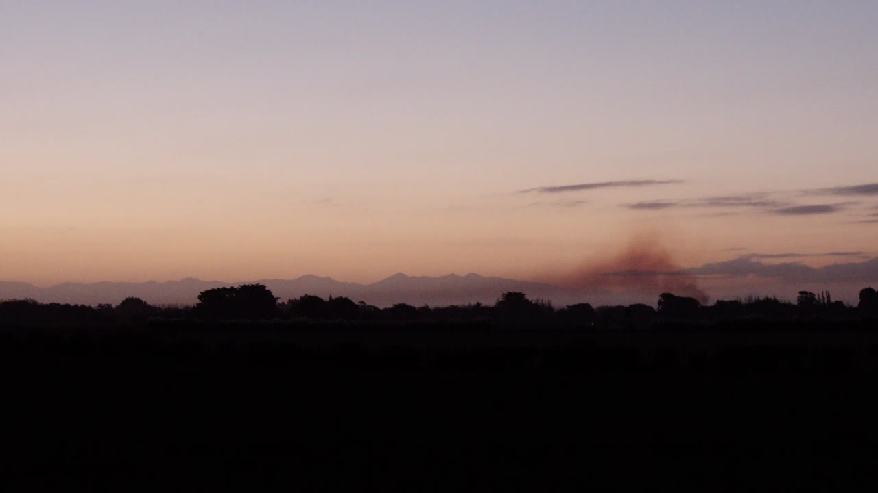 puesta de sol en el campo en nueva zelanda con humo saliendo de la cabaña familiar