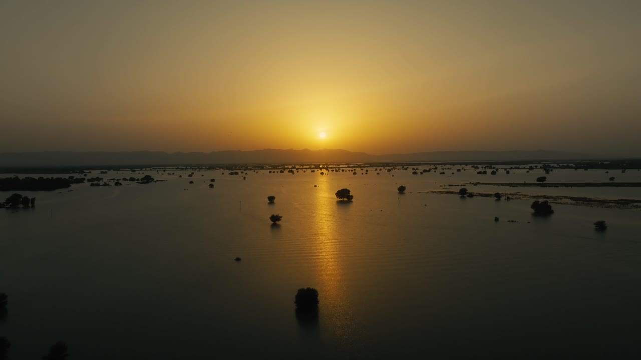 Sunset reflects on expansive floodwater over trees of River Sutlej in Punjab, Pakistan