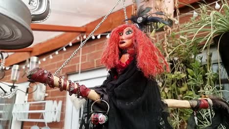 hand crafted red haired witch hanging from broomstick in home garden outdoor shelter