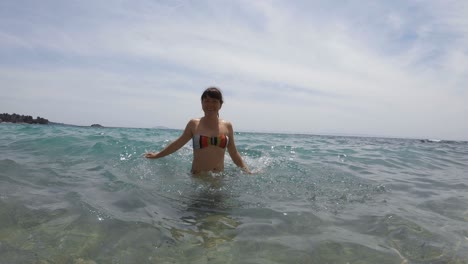 a young woman splashing water in the sea looking at the camera and turning around
