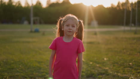 pretty little girl shakes ponytails standing on park meadow