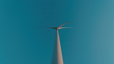 wind turbine blades spinning against a clear blue sky, shot from below, in slow motion