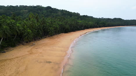 Drone-circling-a-girl-walking-on-the-Praia-Grande-beach-on-Ilha-do-Principe,-Africa