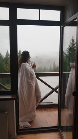 woman enjoying a warm drink with a view of foggy mountains and a lake.