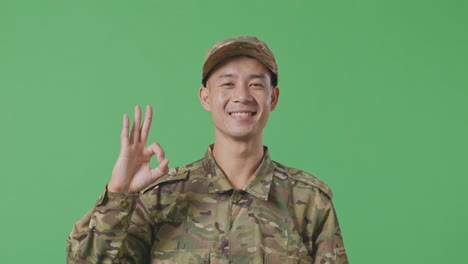 close up of asian man soldier smiling and showing okay gesture to camera while standing in the green screen background studio