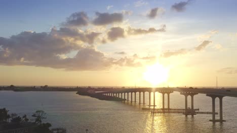 drone 4k wide pullback from bridge at sunset with boat passing