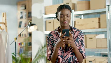 african american designer woman texting on smartphone and leaning on the table in a fashion clothing store