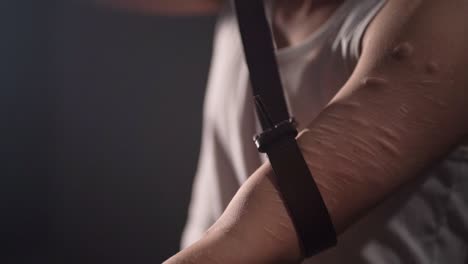 closeup of a man with scars all over the left arm using a leather belt as a tourniquet preparing himself for a intravenous injection