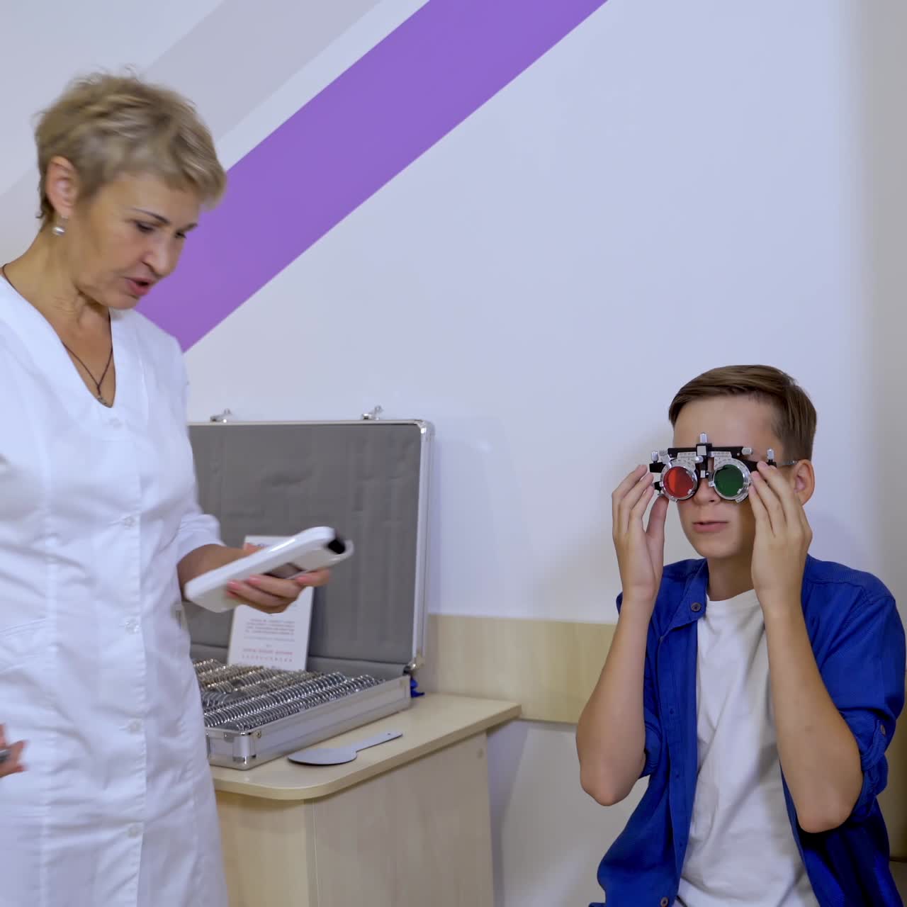 Portrait of a kid boy wearing corrective glasses with replaceable lenses. Ophthalmology clinic. Doctor is checking eyesight of a small male patient