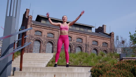 a young beautiful fit woman does jumping jacks outdoors in an urban environment