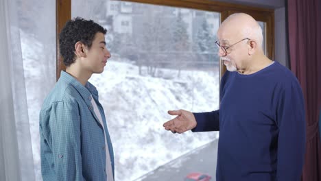 grandfather and grandson looking out the window at home, enjoying the winter snowfall.