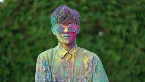 portrait of boy standing being covered in coloured powder at holi festival.