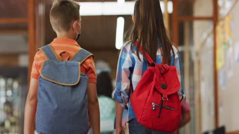 diverse schoolchildren wearing face masks walking through corridor, talking,