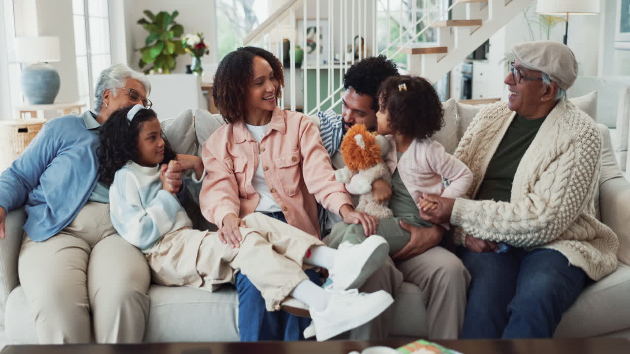 A multi-generational family smiles and laughs together while sitting on a couch in their living room.