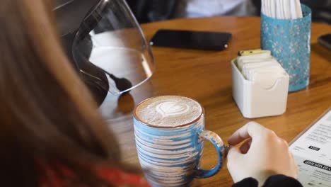 woman with a cup of coffee with latte art on the table during meeting. back view