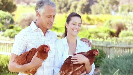 smiling farmer couple holding chickens