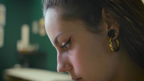 Close-up-of-a-beautiful-young-girl-with-large-earrings-and-makeup-who-is-concentrating-on-tattooing-in-her-studio-and-smiling-in-slow-motion