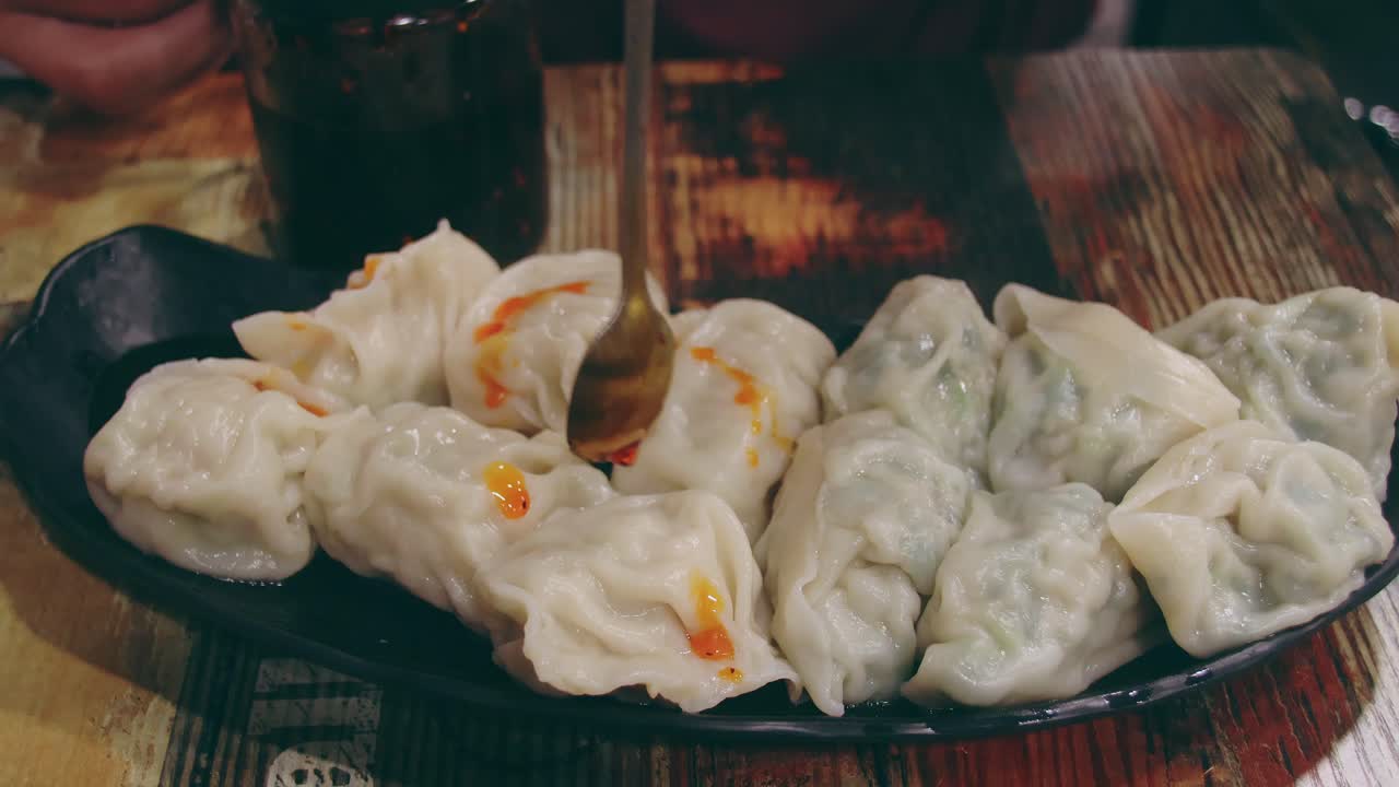 Menuangkan minyak cabai di atas seporsi momo atau pangsit kukus, makanan Nepal tradisional lokal yang otentik di sebuah restoran, pengalaman kuliner jujur.