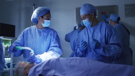 Mixed-race-surgeons-wearing-protective-clothing-looking-at-patient-in-operating-theatre