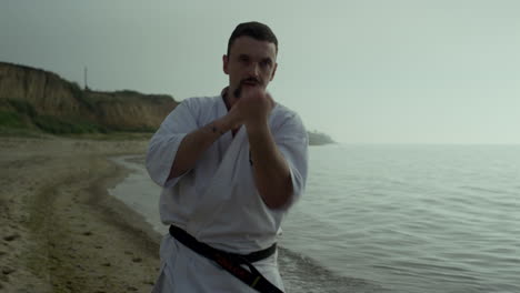 strong fighter exercising punches on beach close up. athlete practicing karate.